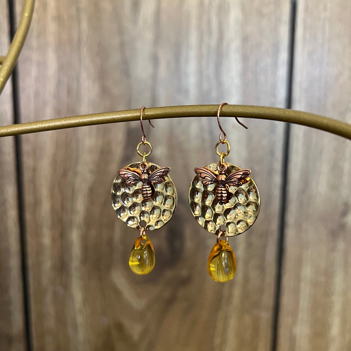 A pair of amber drop honey bee earrings displayed against a wooden background.