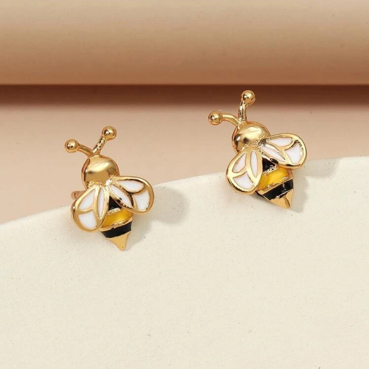 A pair of gold-colored stud earrings featuring a bee motif on a light background.