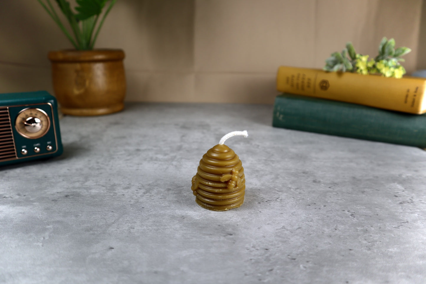 Beeswax candle shaped like a honeycomb on a concrete surface with books and a plant in the background.