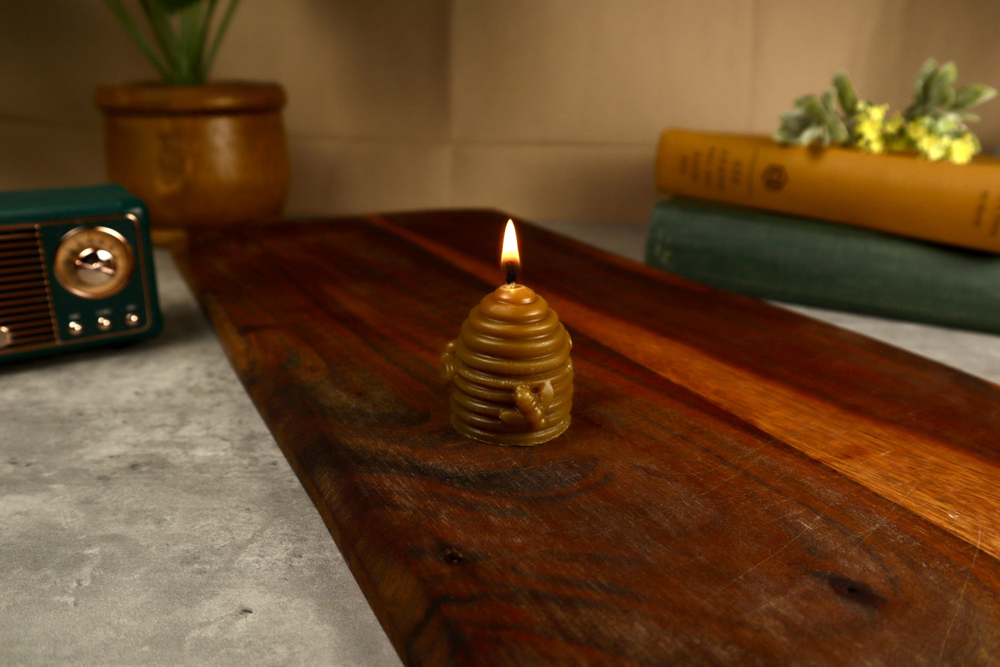 Small lit candle in a decorative holder on a wooden surface with a vintage radio and plants in the background.