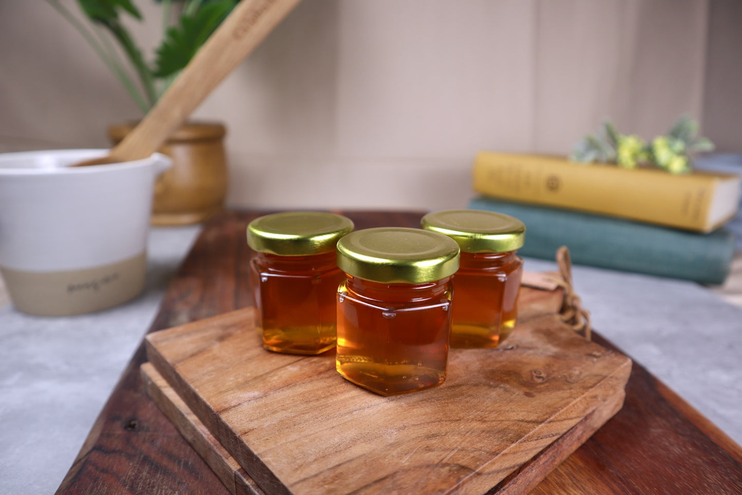 Three jars of honey with gold lids on a wooden cutting board.