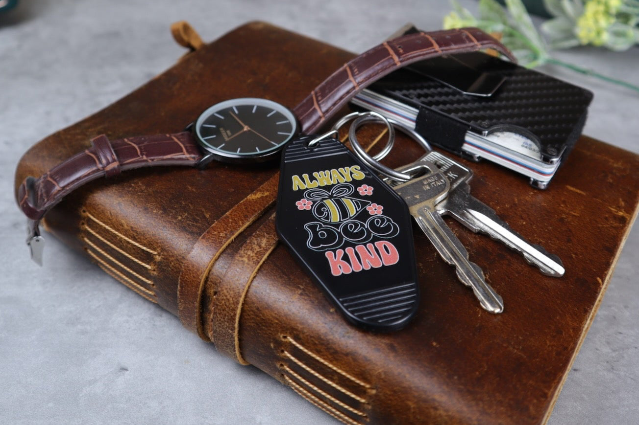 Brown leather journal with keys, watch, and wallet on a gray surface with books and decorative items in the background.