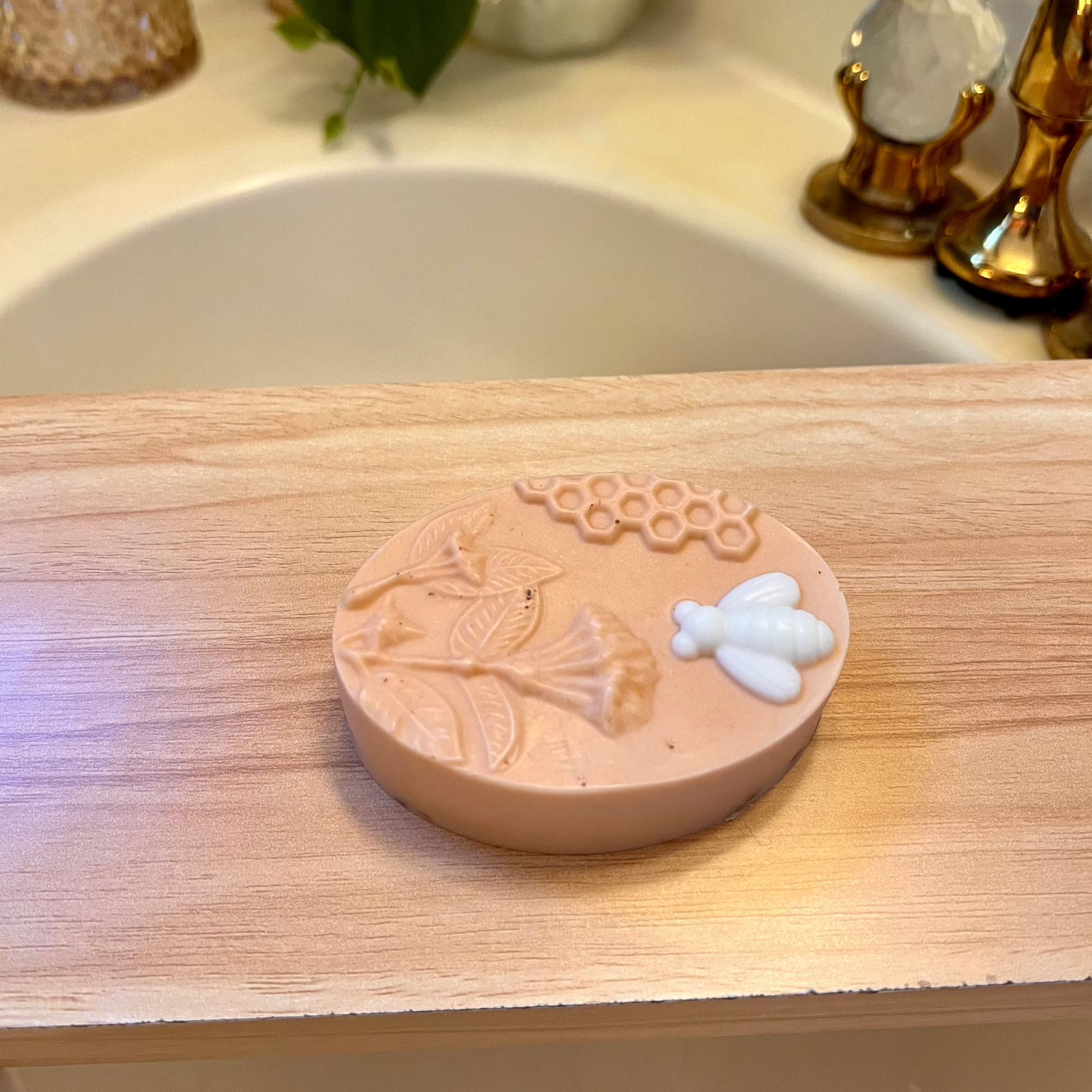 A bar of soap with apple honey cinnamon scent, placed on a wooden surface, with a blurred background suggesting it is in a bathroom setting.